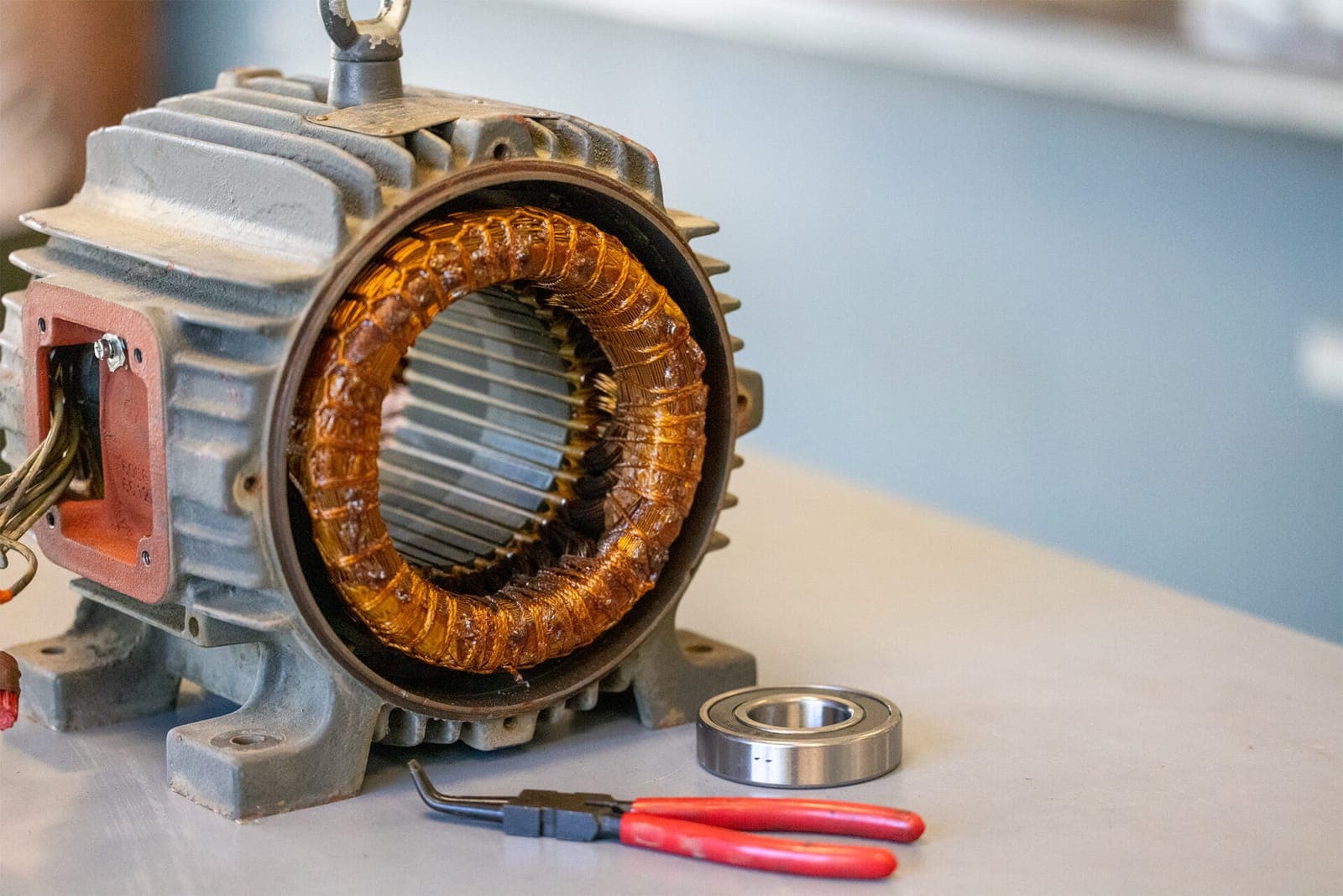 A motor stator being serviced on the workbench with a new bearing and snap-ring pliers